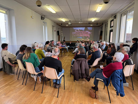 Image de l'assemblée générale de l'association le pilou à prendeignes. Elle re présente un groupe de personnes assises en cercle lors d'une réunion dans une salle lumineuse. Présentation projetée à l'arrière-plan, ambiance sérieuse.