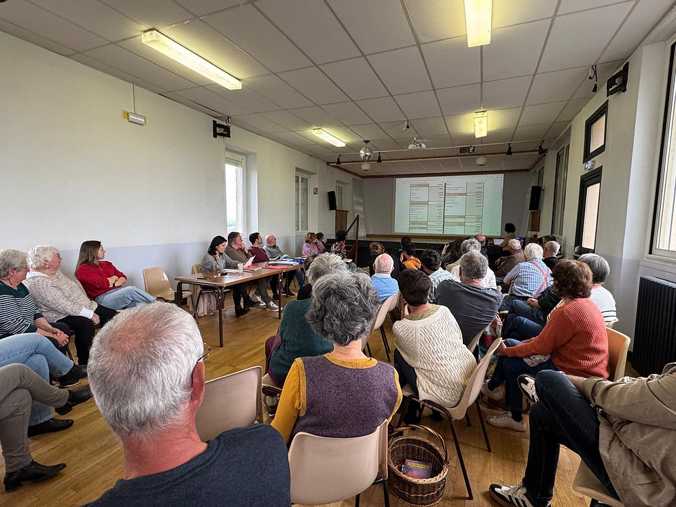 Personnes assises en cercle dans une salle, regardant la projection du bilan financier de l'association le pilou de prendeignes sur un mur. Ambiance studieuse, plafond blanc, paniers en osier au sol.