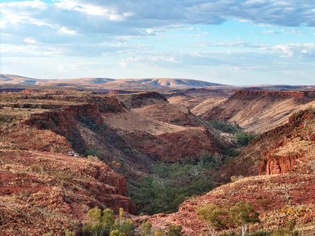Two 4WD vehicles parked on the edge of a deep red rock canyon at Eagle Rock Falls in the Pilbara, with mountain ranges fading into the distance under a partly cloudy sky.