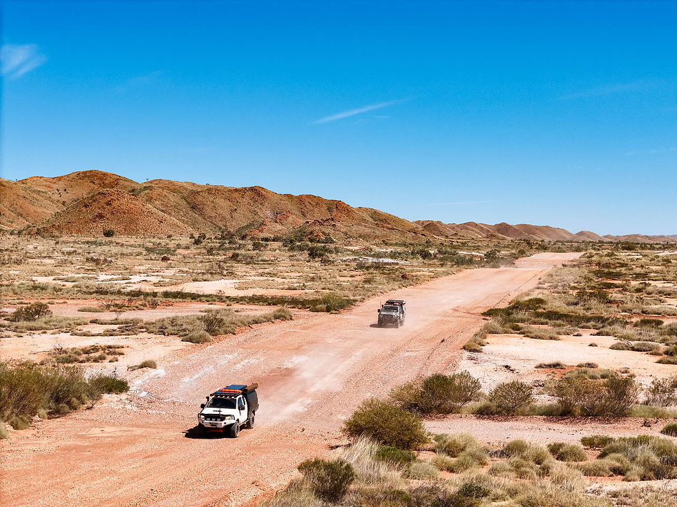 Two 4WDs travelling along the dusty Skull Springs Road in the Pilbara, with red ranges and spinifex country in the background.