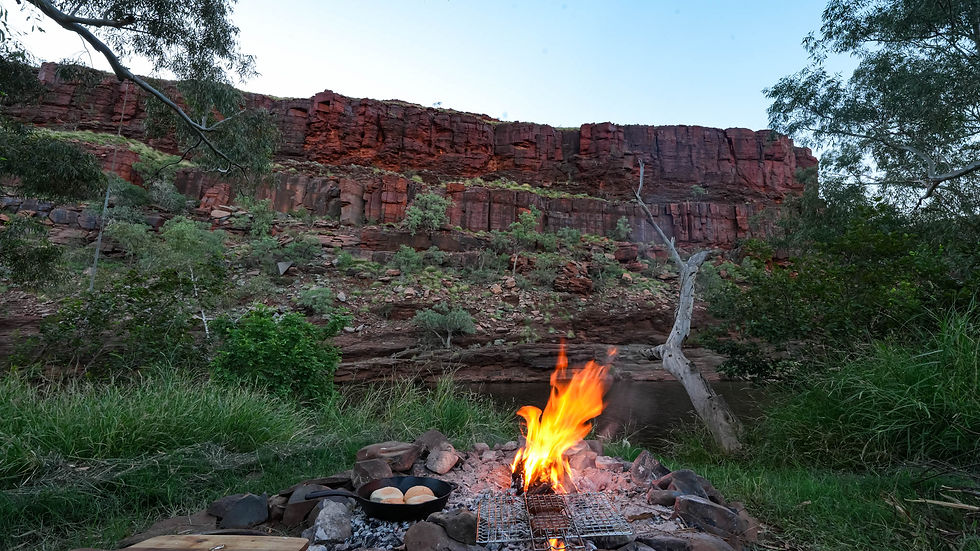 Camp oven cooking on an open fire at George Gorge with sheer red rock cliffs in the background, West Pilbara Western Australia