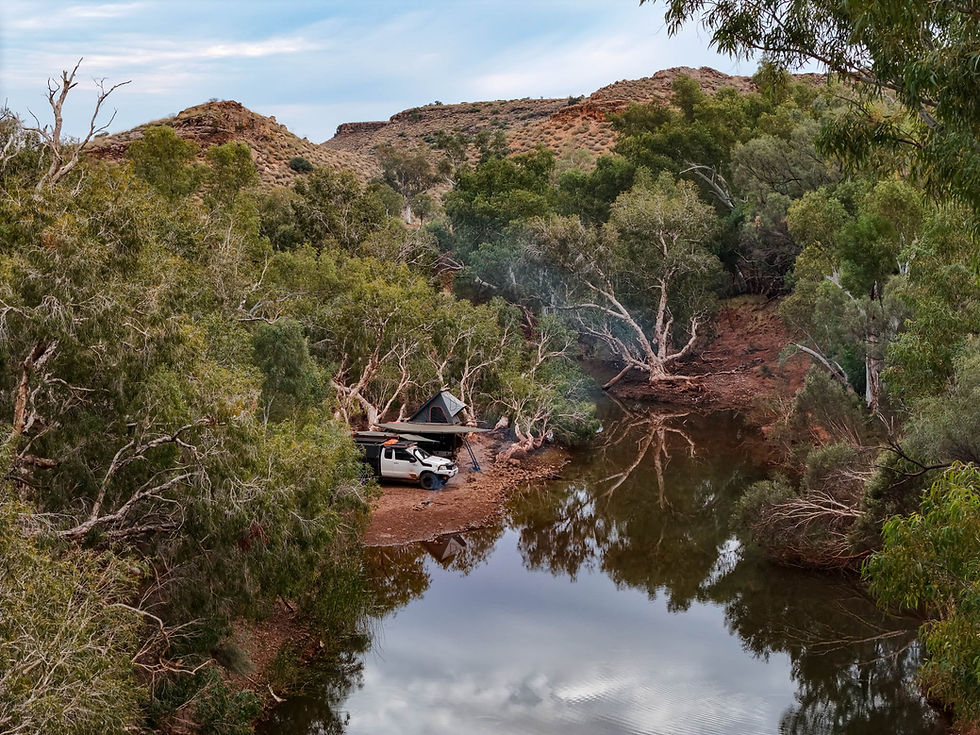 A 4WD with rooftop tent set up beside still water at Eel Pool, with paper barks and reflections of the sky on the surface.