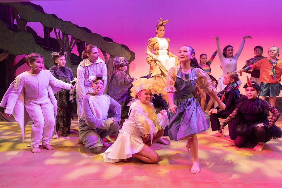 Children in colorful animal costumes perform energetically on stage with a purple and pink backdrop, creating a lively and playful atmosphere.