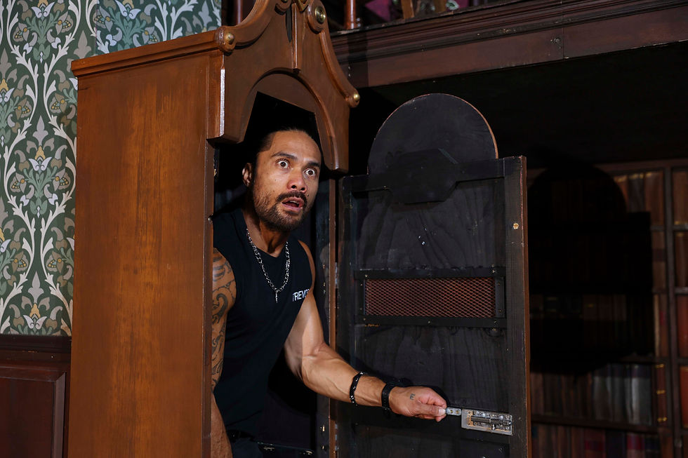 Man with a surprised expression peeking from a secret door in a wooden cabinet, set against patterned wallpaper. He's holding a latch.