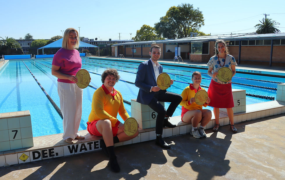 Five people hold gold coins by a pool, some in red and yellow outfits, standing by lanes. "DEE WATER" sign visible. Bright, sunny day.