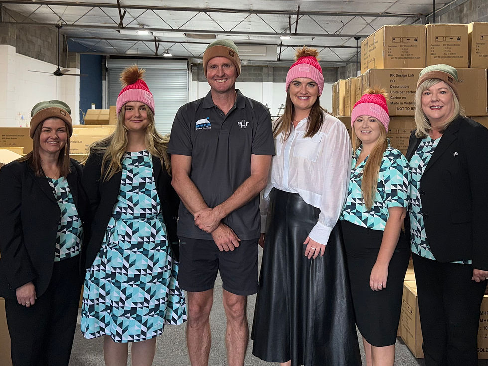 Six people wearing colorful beanies and geometric-patterned outfits stand smiling in a warehouse with stacked cardboard boxes.