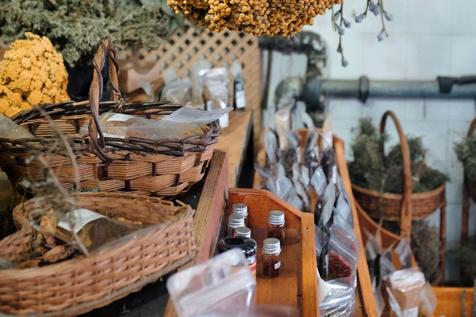 Rustic shop display of wicker baskets, dried flowers and herbs, with small glass bottles on wooden shelves in a cozy, muted interior
