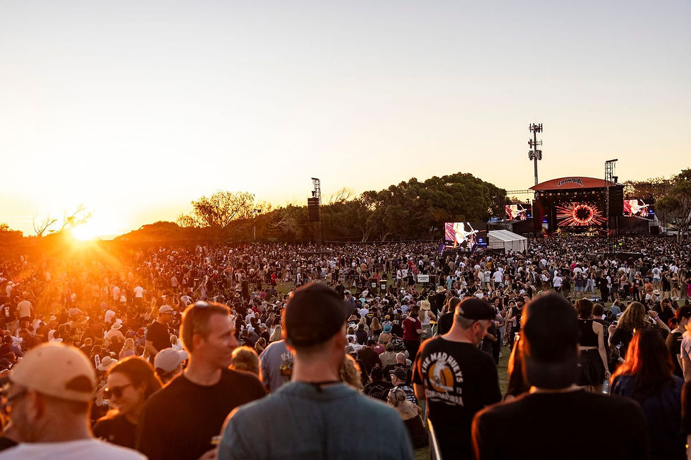 Crowd at outdoor concert during sunset, vibrant stage lights. People enjoying music, relaxed atmosphere. Large screens display visuals.