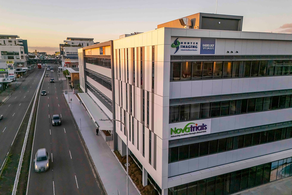 Building with "Hunter Imaging" and "Novatrials" signs at sunset, beside a busy street with cars driving by, creating an urban evening scene.
