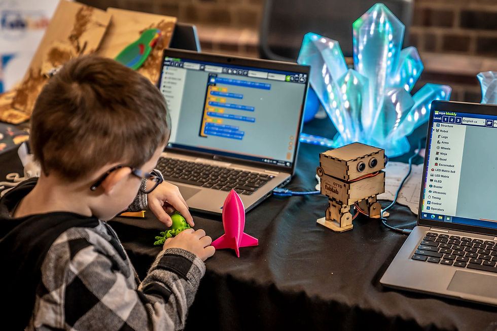 Child explores colorful toy models between two laptops showing coding software; glowing crystal lights in background.