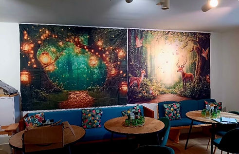 Wandteppich im Kind-Eltern-Bereich des Vivid Café mit verzaubertem Wald, leuchtenden Laternen und einem Hirsch.