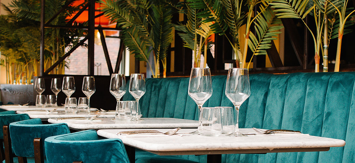 Elegant restaurant interior with tables set for dining, teal seating, and greenery.
