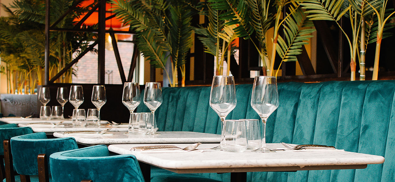 Elegant restaurant interior with tables set for dining, teal seating, and greenery.