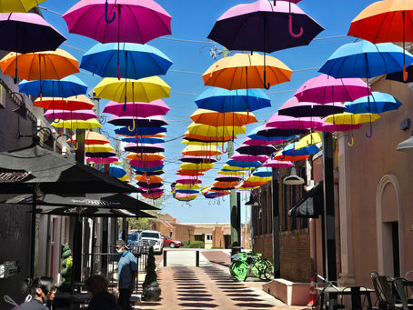 Bright umbrellas strung overhead, suspended from lines that seem to disappear amidst a backdrop of blue sky.