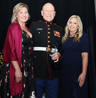 Three people standing together. A military man holding an award. Inspire Gala honors.