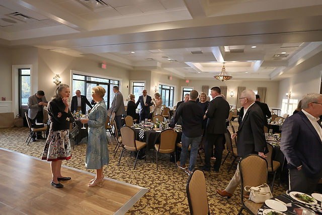 Guests mingling at an event in a ballroom with round tables and decor.