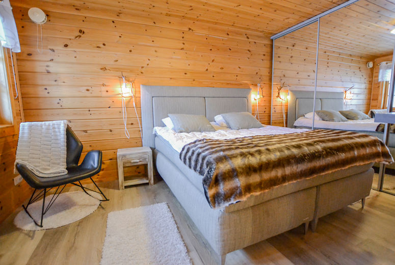 Bedroom with double bed and warm wooden walls inside Lukkohalla log cabin in Ukkohalla Finland.