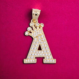Colgante con la letra “A” dorada, con remate de corona, incrustado con circonitas cúbicas blancas sobre fondo magenta.