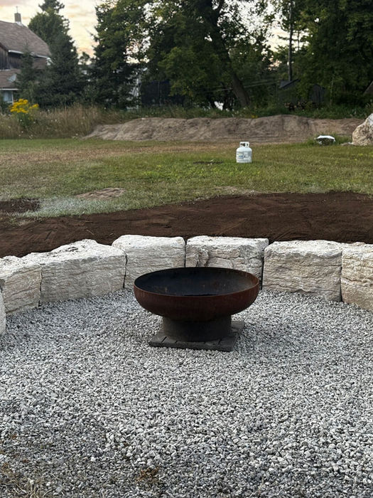 Armour stone curved firepit surround with pebble ground and garden