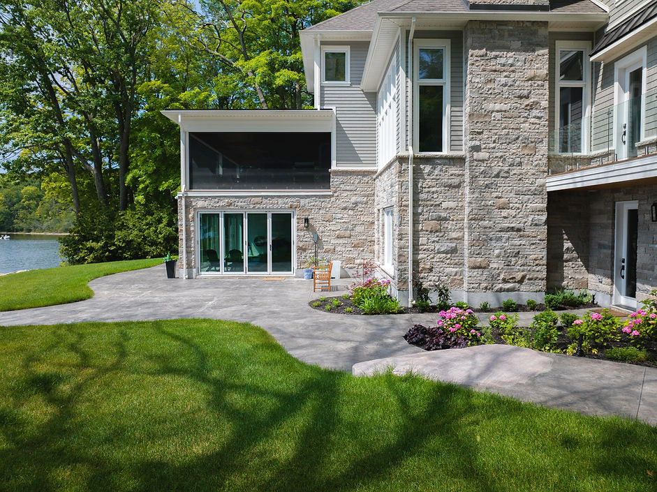 Muskoka lakefront property with off-white brick home, interlocking brick path, grassy backyard, and gardens, designed by Morden Landscaping