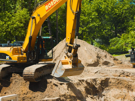 Excavator performing site preparation and grading for construction on a Muskoka property with trees
