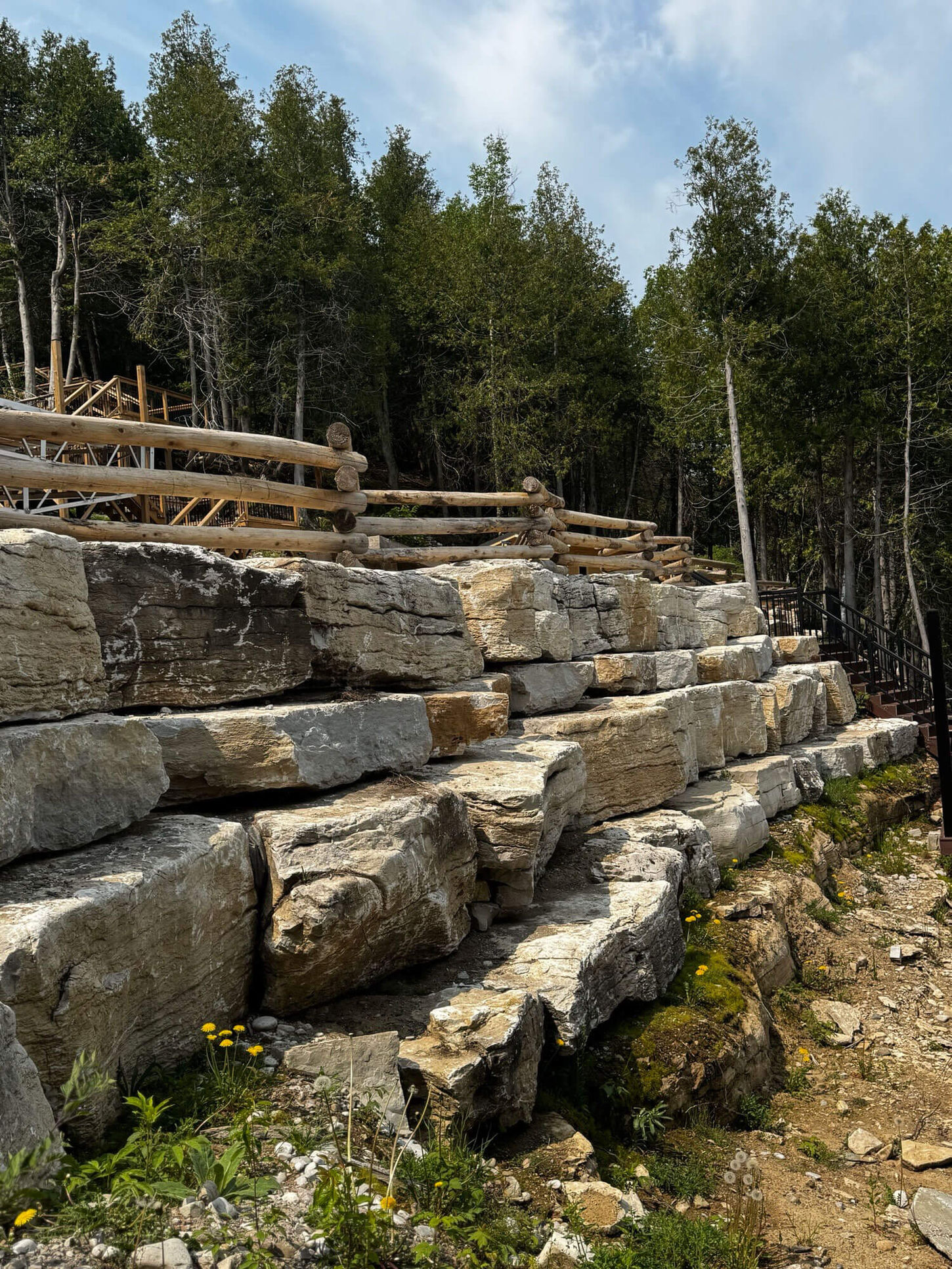 Staggered limestone retaining wall with wood fence and forest