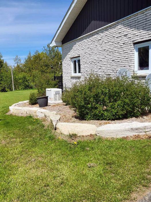 Armour stone garden border alongside grey brick house Ontario