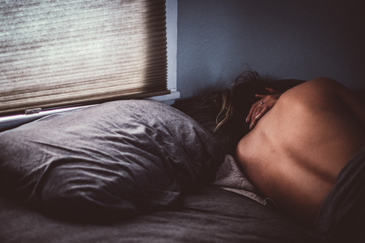 Pessoa adulta na cama, enrolada no lençol e pensativa representando a insegurança com o corpo na intimidade