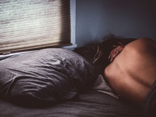 Pessoa adulta na cama, enrolada no lençol e pensativa representando a insegurança com o corpo na intimidade