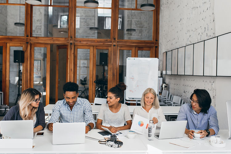 tired-asian-it-specialist-drinking-coffee-watching-female-colleague-working-with-laptop-in