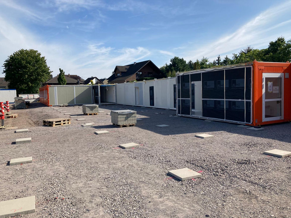 Baustelle mit mehreren Containermodulen in Weiß, Grün und Orange, teilweise noch mit Schutzfolie versehen.