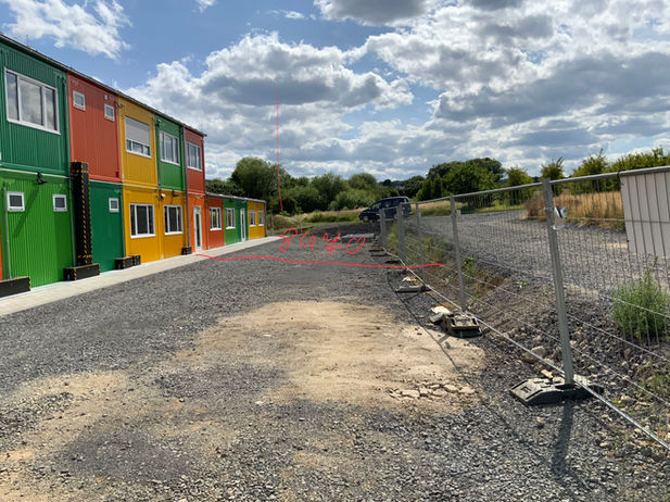 Zweistöckige bunte Containeranlage mit Außentreppe, ein Monteur befestigt das Treppengeländer.