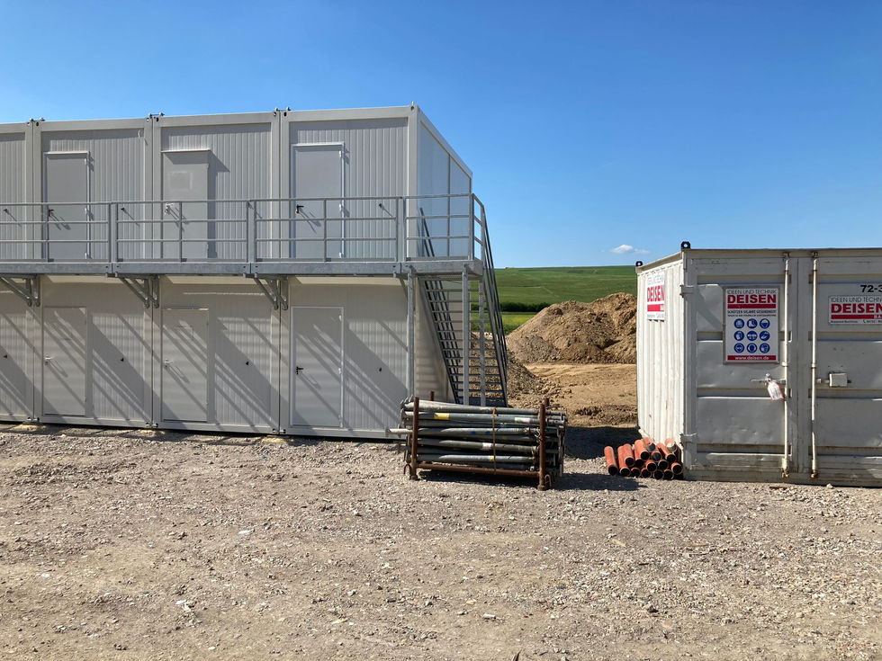 Gebäudeecke einer grauen Containeranlage mit Außentreppe und Baucontainer der Firma Deisen im Vordergrund.
