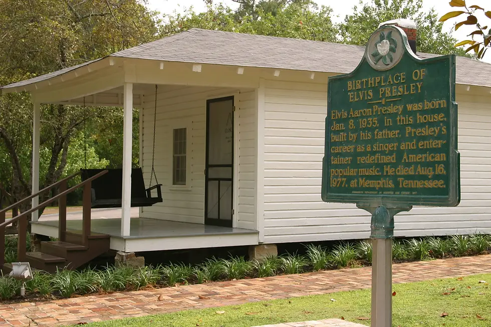 White wooden house with porch swing, surrounded by trees. Green sign reads "Birthplace of Elvis Presley," detailing his birth and career.
