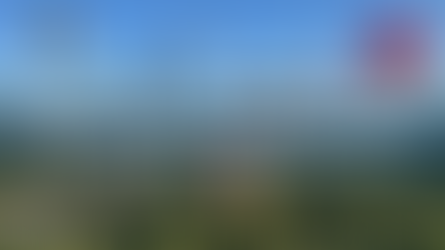 Hot air balloons of various colors float over a river and green landscape under a clear blue sky. Text says, "More Than the Mother Road: New Mexico’s Enchanting Lands."