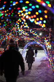 People walk under a tunnel of colorful Christmas lights in a snowy setting, creating a festive, magical atmosphere.