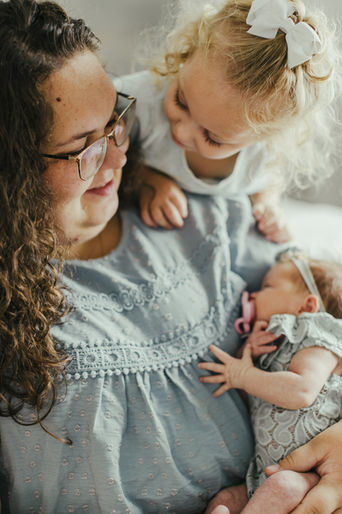 Woman holding baby with toddler looking on; FAMILIES, mother and daughters, in studio.