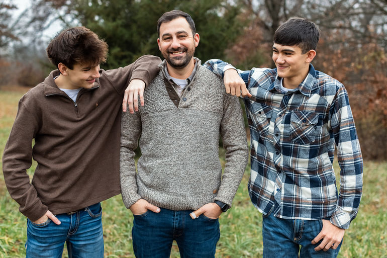 Dad with 2 sons, one on each side of him with their elbows on his shoulders
