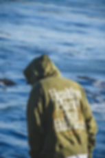 person standing at the shoreline wearing Coastal Sun hoodie with the hood up