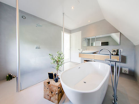 Fugenloses Bad, Betonoptik, Waschtisch mit aufgesetzem Waschtbecken, Wasserhahn, Dusche mit Unterputzgarnitur, Spiegel, Glasduschabtrennung, freistehende Badewanne, Pfalnze, warme mediterrane Farbtöne