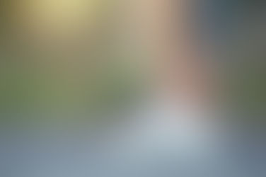 Person in gray leggings holds their ankle in one hand, wearing white sneakers on a path. Background is blurred with soft greenery.