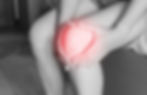 Person holding their knee with both hands. Knee is highlighted in red, suggesting pain. Background shows a bed and floor tiles.