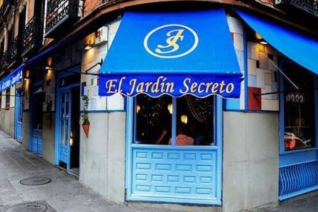 Blue storefront with an awning reading "El Jardín Secreto." Set on a street corner, with plants and warm interior lights visible.
