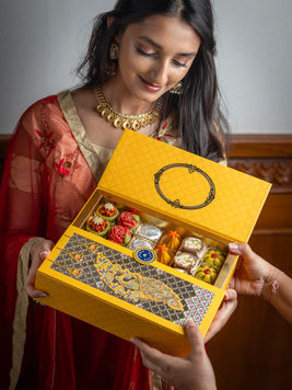 Elegant woman in traditional dress holding a luxury Indian sweets box, perfect visual for festive restaurant reviews and dining stories.