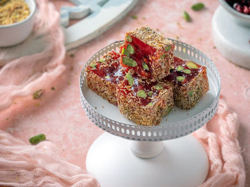 roles food photographer in styling pistachio dessert cubes on stand with pink fabric and props, showing vivid colour and texture