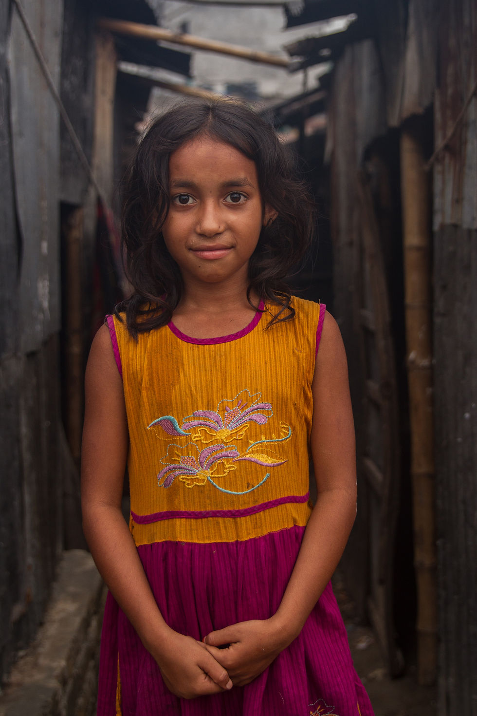 Street Photography Documentary portrait of a young girl in a colorful dress, standing in an alleyway with natural light and honest expression.