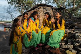 social documentary photography of village girls in yellow and green dresses laughing together on stone wall at sunset
