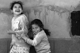 Documentary photo, black-and-white of two laughing girls playing against a rough wall—candid expressions, joy, and innocence.