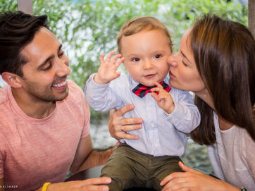 Documentary family photographer captures parents cuddling and kissing their toddler in a candid, joyful moment full of real connection