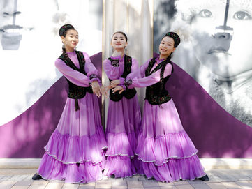 Creative Event Photographer capturing three dancers in lilac traditional dresses posing together at a cultural festival in front of an artistic backdrop